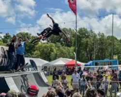 A BMX rider performing an aerial trick over a ramp at an outdoor skate festival.