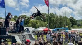A BMX rider performing an aerial trick over a ramp at an outdoor skate festival.