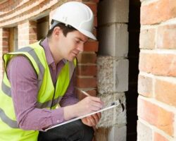 Inspector in safety gear records observations beside an exposed brick wall