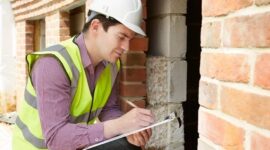 Inspector in safety gear records observations beside an exposed brick wall