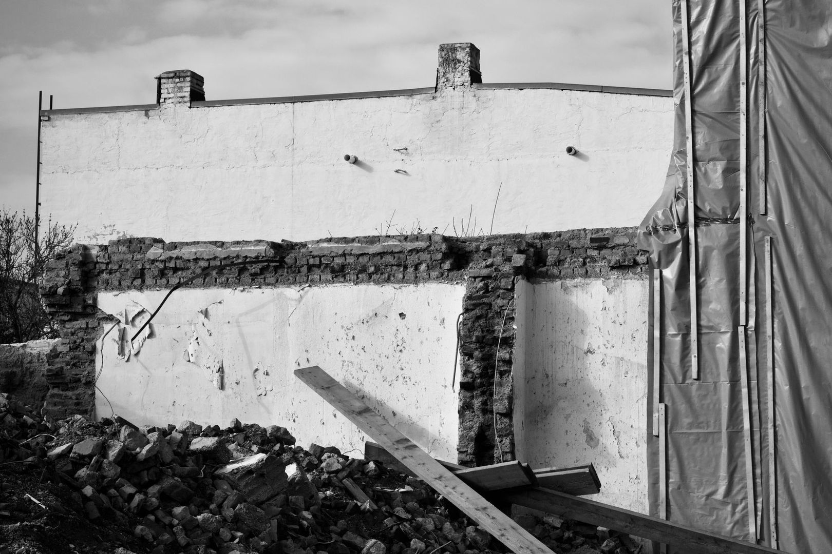 Partially demolished masonry wall with rubble and temporary sheeting