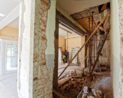 Workers selectively dismantling an interior with exposed brick, beams, and debris