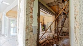 Workers selectively dismantling an interior with exposed brick, beams, and debris